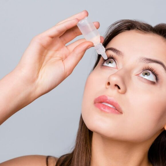 Image shows woman looking up putting eye drop in eye